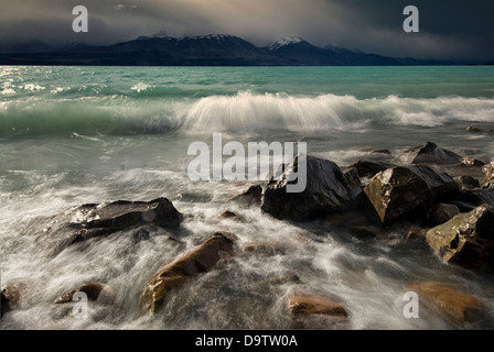 Wellen am felsigen Ufer des Lake Pukaki, mit dunklen Wolken über den Bergen hängen. Neuseeland Stockfoto