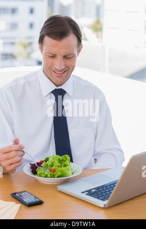 Lächelnde Geschäftsmann Essen einen Salat auf seinem Schreibtisch Stockfoto