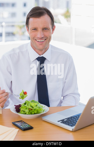 Fröhliche Geschäftsmann Essen einen Salat auf seinem Schreibtisch Stockfoto