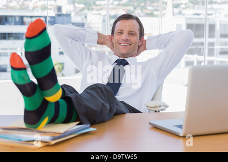 Lächelnd Geschäftsmann entspannend mit Füßen auf seinem Schreibtisch Stockfoto