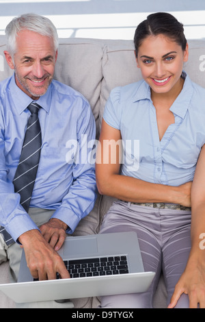 Geschäftsleute mit Laptop auf der Couch und lächelte Kamera Stockfoto