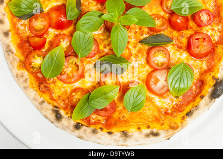 Pizza mit Tomaten und Basilikum Blätter auf einem weißen Teller. Stockfoto