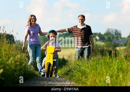 Familie mit jungen Kind einen Wochenendausflug, die Eltern während der Sohn Praktiken ein Training Fahrrad gehen auf Stockfoto