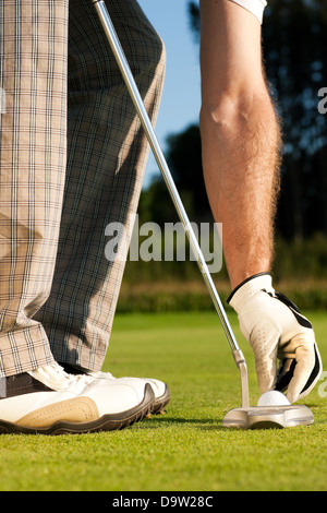 Anpassung des Golfballs vor dem Loch Mann bereit, den Cup zu schlagen, er trägt einen Handschuh Stockfoto