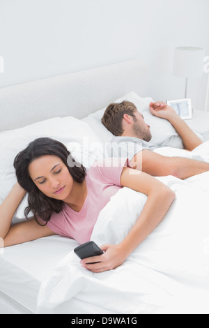 Frau von SMS-Nachrichten im Bett, während ihr Mann schläft Stockfoto