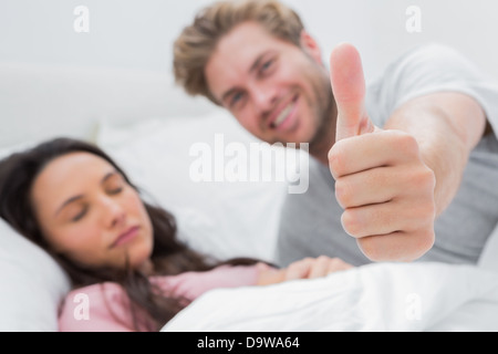Mann Daumen aufgeben, während seine Frau schläft Stockfoto