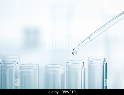 Eine Nahaufnahme von einer Labor-Glas-Pipette mit aufstrebenden Tropfen Substance over eines mehrere Reagenzgläser auf hellem Hintergrund Stockfoto