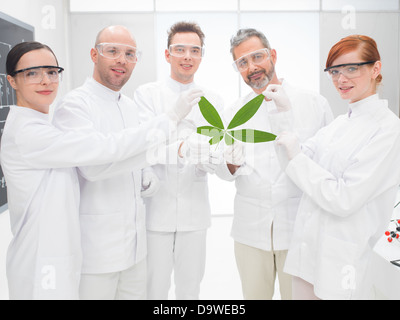 Gruppe von fünf männliche und weibliche Wissenschaftler hält eine gentechnisch veränderte Blatt in eine Genetik Labor lächelnd proudl Stockfoto