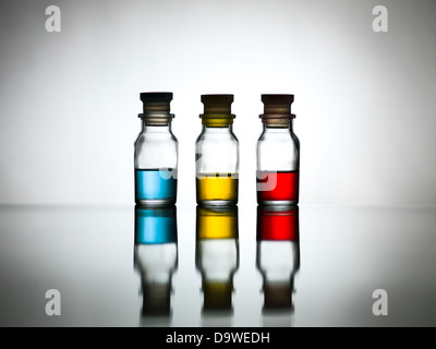 Beleuchtung und grauen Hintergrund mit drei geschlossen kleine Flaschen mit verschiedenen flüssigen Farben: blau, gelb, rot und ihre Reflexion auf dem Tisch Stockfoto