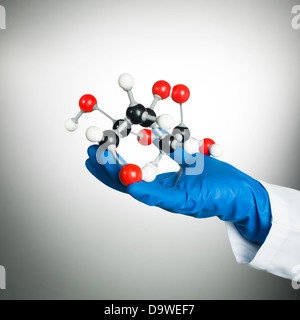 in blaue Gummihandschuh die Hand und weißen Kittel ein 3d Modell einer Mollecular-Struktur aus weißen, schwarzen und roten Kugeln mit grauen Anleihen gegen einen Farbverlauf weiß auf grauem Hintergrund Stockfoto