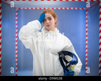 rothaarige Frau in weißen Schutzanzug einen Schutzhelm in eine Hand und wischte ihre Stirn mit den anderen Stockfoto