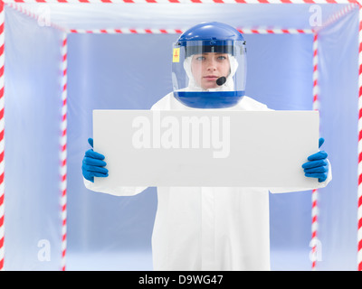 Person im Schutzanzug und Helm präsentiert eine weiße Tafel mit beiden Armen vor einer Entbindung Zelt Stockfoto