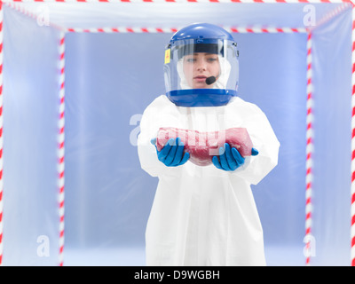 Person im Biohazard Klage anrufen, halten Sie ein Stück rohes Fleisch mit beiden Händen vor der ein Containment-Zelt Stockfoto