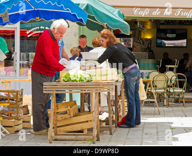 Helles, sonnenüberflutete Bild von Kunden, die an einem Verkaufsstand für Gemüse im Place du Coderc, Perigueux, Frankreich, Produkte auswählen Stockfoto