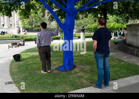 London, UK. 27. Juni 2013. Festival-Gärten, City of London. Menschen interagieren Sie mit einer der Bäume, die als Teil der blauen Bäume in London Kunstinstallation blau gemalt. Nächstenliebe Bäume für Städte gemeinsam mit internationalen Künstler, Konstantin Dimopoulos, kam mit dem Blue Tree-Konzept. Die Idee des Projekts ist es, Menschen zu stoppen und beachten Sie die Bäume im städtischen Umfeld. Wenn Stadtbevölkerung wächst, verringert sich die Anzahl der Bäume in der Stadt. Aber viele Menschen heute um zu betrachten, berühren und Foto eines der blauen Bäume gestoppt. Bildnachweis: Allsorts Stock Foto/Alamy Live-Nachrichten Stockfoto