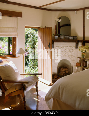 Weißen Kissen auf Holzstuhl im Ferienhaus Schlafzimmer mit weißen Kamin neben der Tür zum Garten Stockfoto