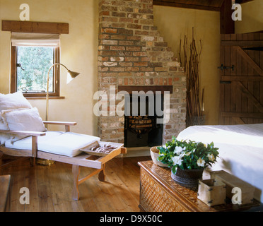Weißen Kissen auf hölzernen liege im Land Schlafzimmer mit Backstein-Kamin und eingelegten Holzkiste Stockfoto