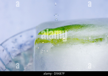 Wasser Tropfen fallen auf eine grüne Chilischote in einen Eiswürfel eingefroren Stockfoto