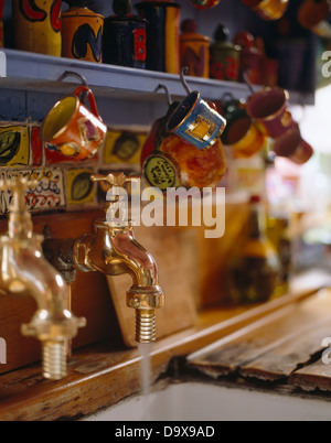 Nahaufnahme von Keramik Becher hängen aus Regal über alte altmodische Messing-Armatur mit Wasser ins Waschbecken laufen Stockfoto