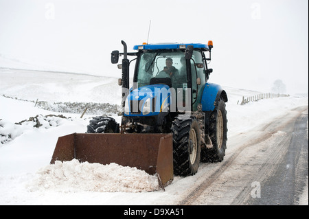 Landwirt auf einem New Holland Traktor aufräumen Schnee Oiff Landstraße nach einem Schneesturm. Cumbria, UK. Stockfoto