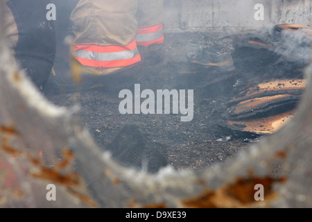 Feuerwehrleute bei einer Feuer-Szene in einem geschmolzenen Gewächshaus bauen mit Rauchen Glut um die Firemans Stiefel Stockfoto