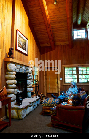 Frau auf Laptop-Computer hoch gewölbte Decke Mauerwerk Kamin bequemen Sesseln Gast Arbeitsraum Gold River Lodge Stockfoto