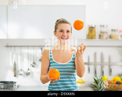 Glückliche junge Frau joggling mit Orangen in Küche Stockfoto
