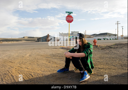 Teenager-Mädchen mit Skateboard sitzt auf der Straße trägt Obey Cap und grün kariertes Hemd, Green River, Utah, USA. Stockfoto