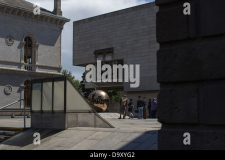 Menschen stehen in einem Innenhof zwischen historischen und modernen Steinbauten in Dublin, Irland, 2013, in der Nähe einer reflektierenden Bronzesphäre. Stockfoto
