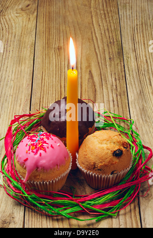 Drei kleine Kuchen und eine brennende Kerze auf einem Holztisch Stockfoto