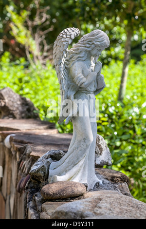 Eine kleine Gartenstatue eine nachdenkliche oder beten Engel sitzt auf einer niedrigen Stein Gartenmauer in Kanapaha Gärten thront. Stockfoto