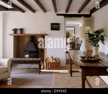 Alter Eichentisch und Holzboden im Weißen Haus Wohnzimmer mit gepolsterten Hocker Kamin mit Holzofen Stockfoto