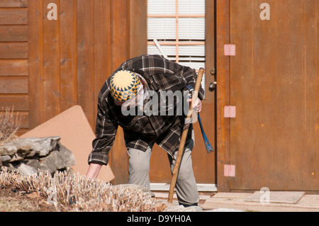 Alter Mann einen Kufi-Hut mit einem Stock und Werkzeug bei der Gartenarbeit Stockfoto