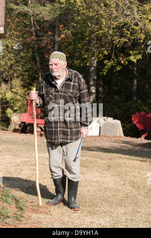 Alter Mann einen Kufi-Hut mit einem Stock und Werkzeug Blick in die Kamera, zu Fuß in seinem Garten Stockfoto