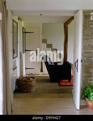 Ferienhaus-Saal mit Blick durch die offene Tür, Ledersessel und großen Log Korb im Wohnzimmer Stockfoto