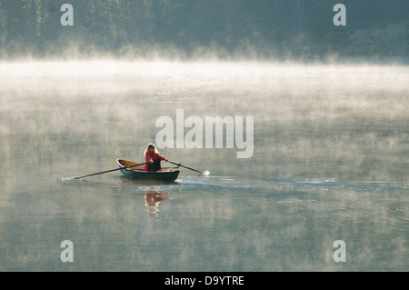 Eine Frau, die ein Scull Rudern Boot einen nebligen Morgen in der Nähe von Creede, Colorado. Stockfoto