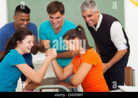 fröhliche weibliche Schülerinnen und Schüler spielen Armdrücken im Klassenzimmer Stockfoto