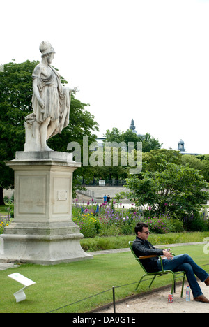 Ein Mann entspannt auf einem Stuhl in der Jardin des Tuileries, Paris, als nächstes eine Statue des Perikles, demokratische Kaiser des alten Athen. Stockfoto