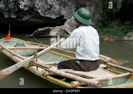 Vietnamesische Mann traditionellen grünen Helm zu tragen und sitzt im Ruderboot in der Nähe der Höhlen von Tam Coc, Provinz Ninh Binh, Vietnam Stockfoto