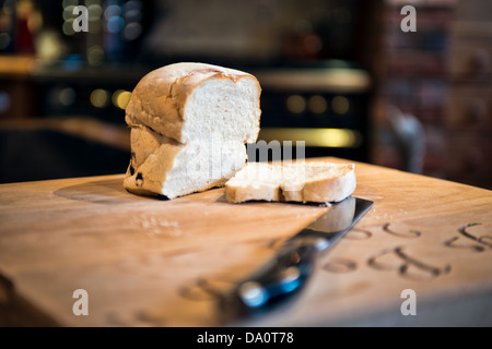 Ein Geschnetzeltes Laib Weißbrot auf einem Steckbrett mit einer de-fokussierten Tranchiermesser in einem Land Küche Stockfoto