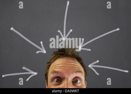 Mans Kopf mit einem gestressten Ausdruck vor einer Tafel mit Pfeilen auf ihn. Stockfoto