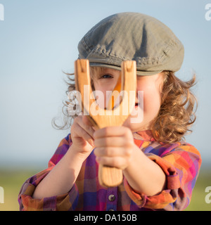 Lustige Kinder schießen hölzerne Schleuder gegen blauen Himmelshintergrund. Stockfoto