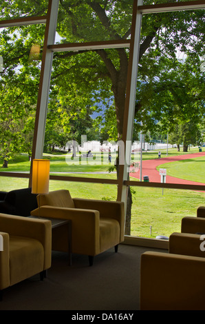 Blick auf ein Feld im Confederation Park von Burnaby-Bibliothek.  Stühle-Silhouette gegen ein Fenster mit Park und die Berge. Stockfoto