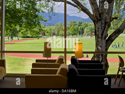 Stühle und Lampen der Burnaby Public Library mit einem Fenster mit Blick auf einen Park, Bäume und Berge. Aktive Menschen im Park. Stockfoto