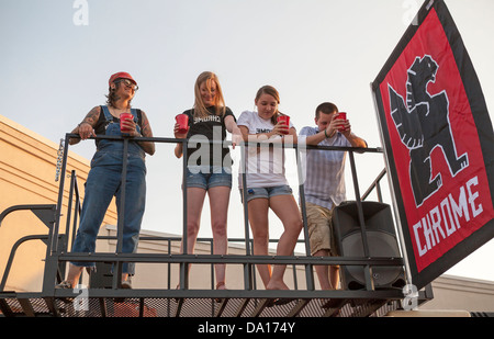 Drei Frauen und ein Mann haben Getränke stehen auf einer erhöhten Plattform. Stockfoto
