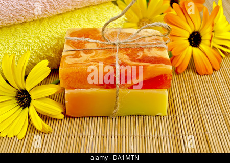 Zwei Bars selbstgemachte Seife gelb und Orange, Handtücher, Ringelblumen auf einem Hintergrund von Bambus-Servietten Stockfoto
