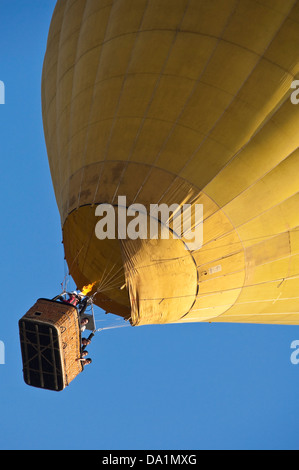 Vertikale Ansicht eines gelb Heißluft-Ballon im Flug mit Passagieren vor blauem Himmel. Stockfoto