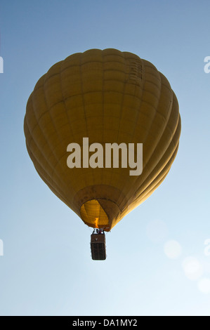 Vertikale Ansicht eines gelb Heißluft-Ballon im Flug mit Passagieren vor blauem Himmel. Stockfoto