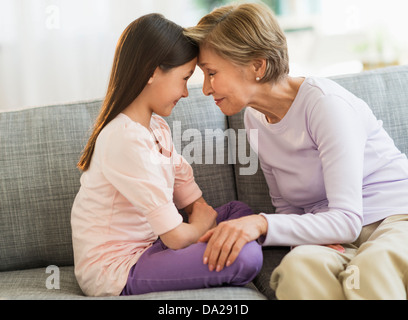 Enkelin (8-9) und Großmutter sitzt auf dem Sofa und berühren mit Köpfen Stockfoto