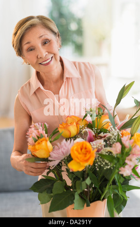Ältere Frau, die Vermittlung von Blumen im Wohnzimmer Stockfoto